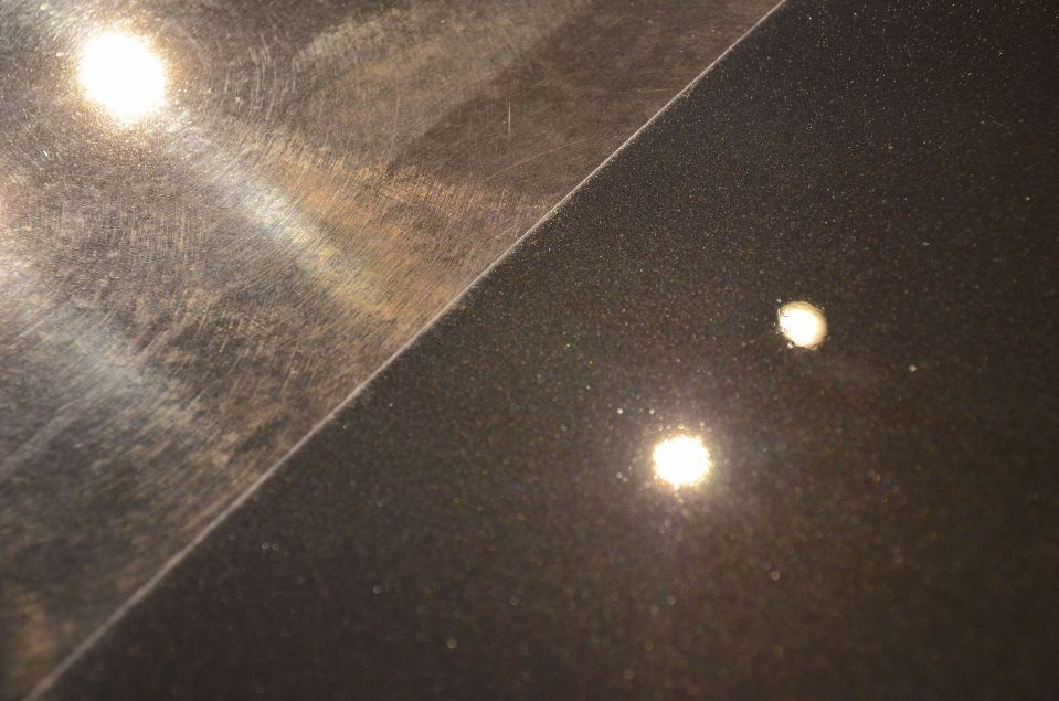 精密研磨によって無数の洗車傷が消え、塗装本来の深い輝きが半分だけ復元された黒い車のボディ比較画像